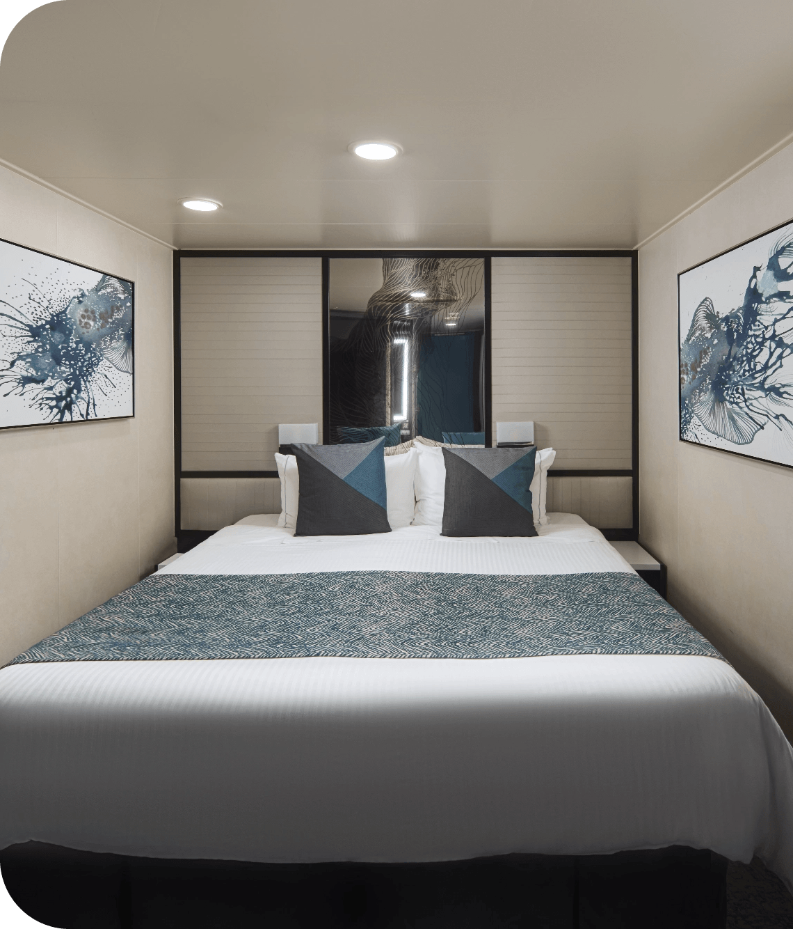 Hotel-style bedroom with a large bed, white linens, and teal-accent pillows facing a panel headboard area. Two abstract blue wall art pieces flank the bed.
