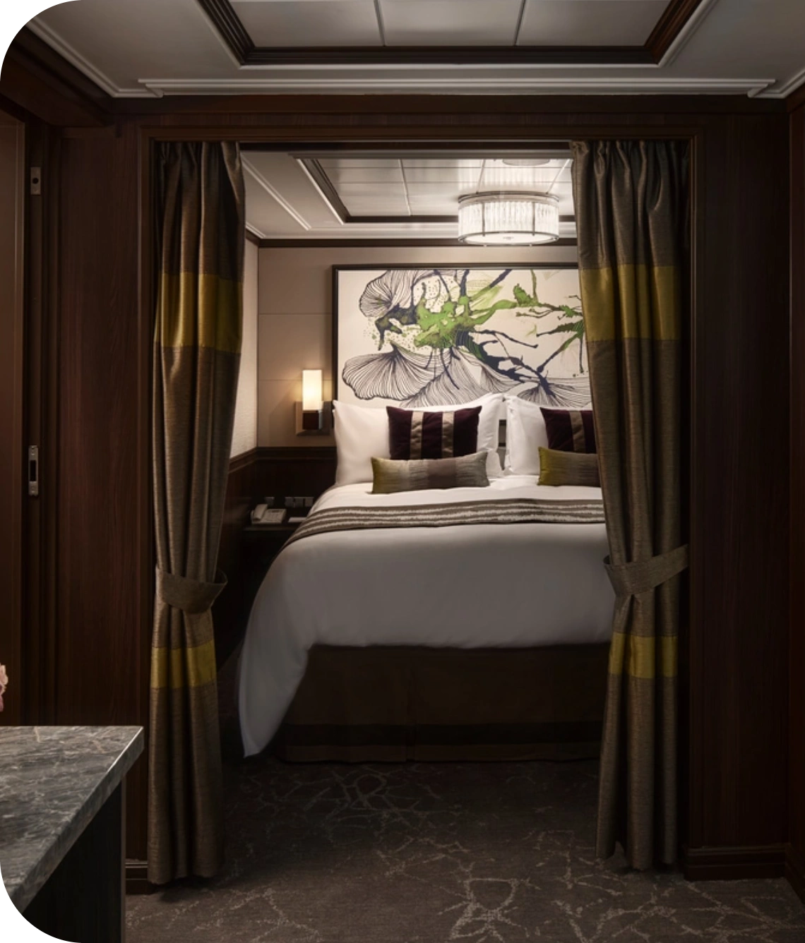 Hotel bedroom viewed through a doorway with dark wood panels, heavy curtains, and a large botanical artwork above the bed.”